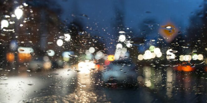 Wie kann man bei Regen fahren. Auto auf der Straße durch Glas gesehen, unscharf.
