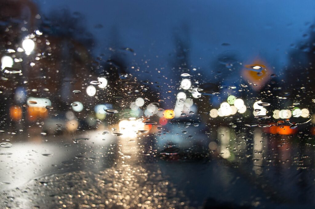 Wie kann man bei Regen fahren. Auto auf der Straße durch Glas gesehen, unscharf.